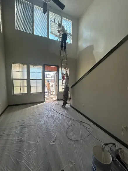Jae Painter Phoenix crew spray painting a two-story living room in Phoenix with floors fully masked